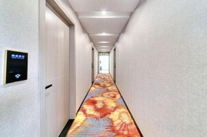 A hotel hallway with a digital sign, a carpet with a floral pattern, and a door at the end.