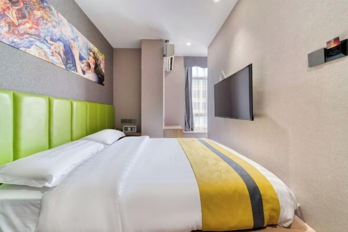 Une chambre d’hôtel avec un lit, un tableau au mur, une télévision et une fenêtre avec des rideaux.