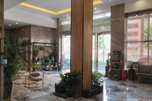 Un vestíbulo con suelo de mármol, amplias columnas de madera y plantas en macetas.