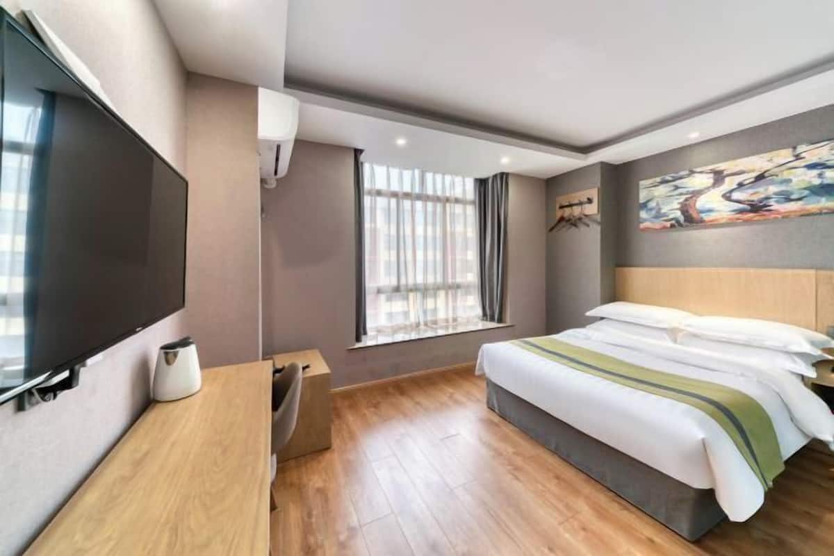 Une chambre d’hôtel moderne dotée d’un grand téléviseur à écran plat, d’un bureau en bois, d’un lit avec une literie blanche et d’une grande fenêtre avec des rideaux.