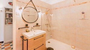 A modern bathroom with a round mirror, a white sink, and a shower. - Bright Apartment in Marseille (Marseille)