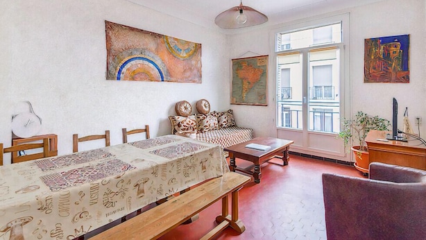 A dining area with a long table, chairs, a sofa, and a bench. There are paintings on the walls and a window with a view. - Bright Apartment in Marseille (Marseille)
