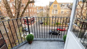 A balcony with a metal railing, potted plants, and a view of a street with cars and buildings. - Hampstead Lux Flat-Hosted by Sweetstay (London)