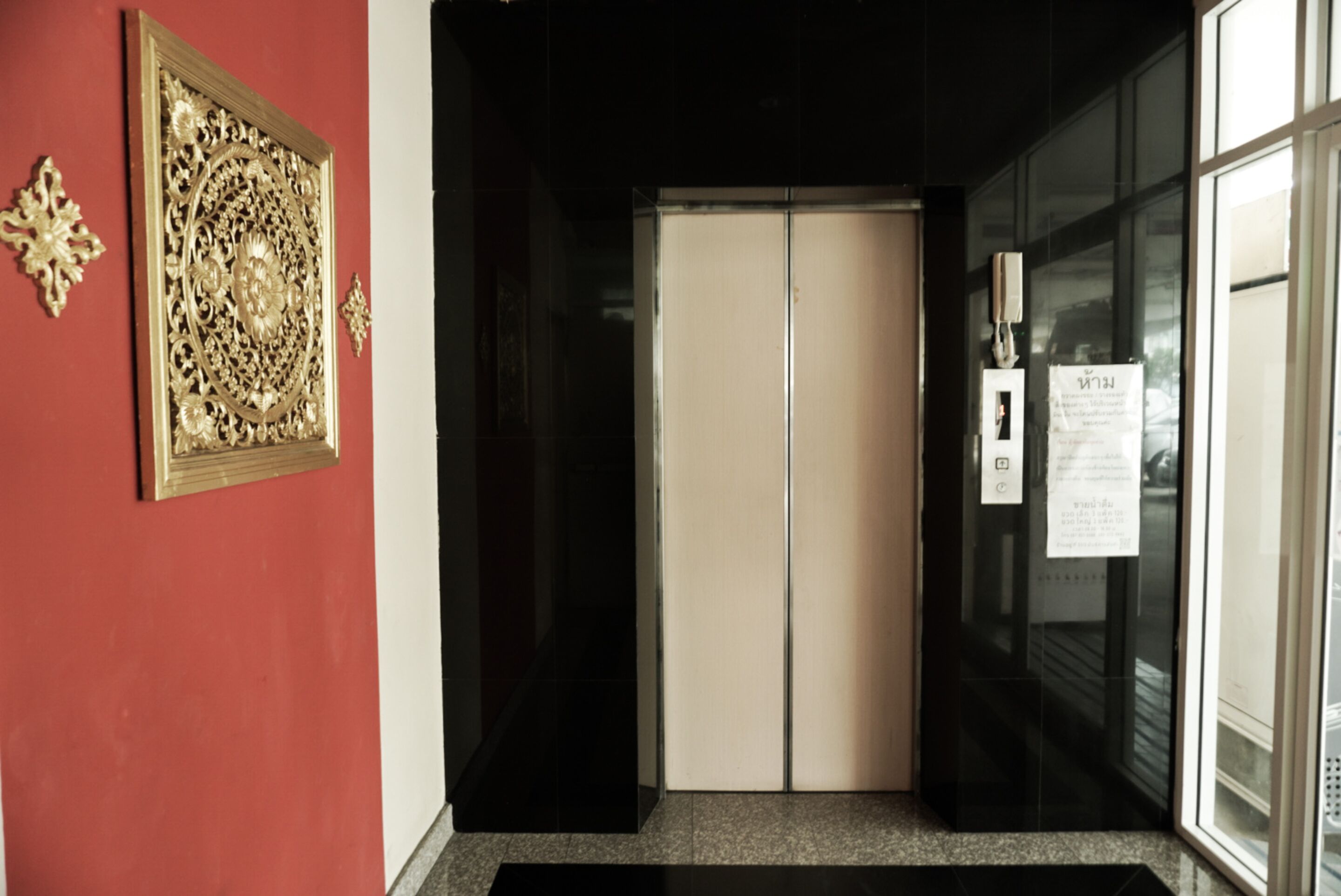 A hallway with a red wall, a decorative gold plaque, and a door leading to a room.