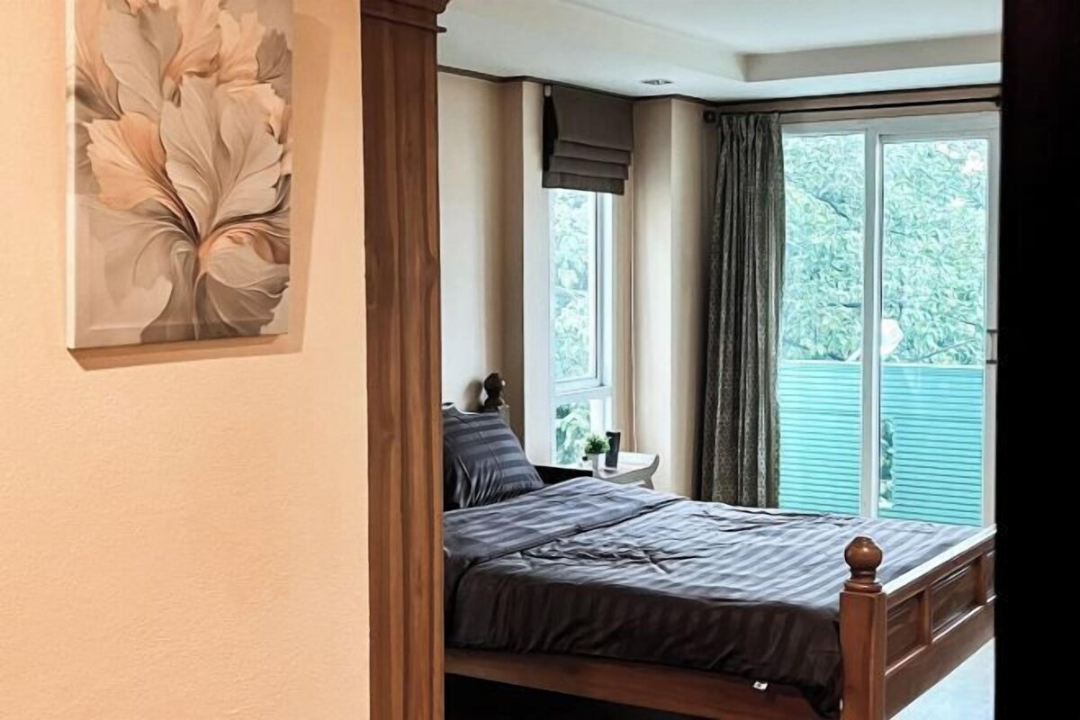 A bedroom with a bed, a nightstand, a window with curtains, and a wall-mounted artwork.