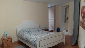 Un dormitorio con una cama individual, una mesita de noche, una lámpara y un florero sobre un tocador.