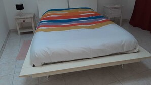 Una cama con colchón blanco y manta a rayas de colores, dos mesitas de noche con lámparas y una cortina roja.