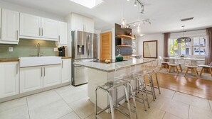 A modern kitchen with white cabinets, stainless steel appliances, and a central island with bar stools. - Silver Palms - Holiday in Style: Beach + Pool! (St. Augustine Beach)