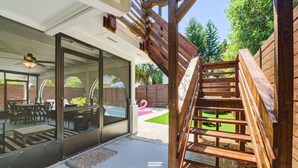 A wooden staircase leading to a patio area with a glass door entrance, outdoor furniture, and a pool. - Silver Palms - Holiday in Style: Beach + Pool! (St. Augustine Beach)