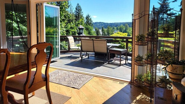 A sunlit room with a large window, a dining table with chairs, and a balcony with outdoor furniture. - Vintage Poulsbo Apartment with Bay views (Poulsbo)