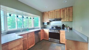 A modern kitchen with wooden cabinets, a stainless steel stove, and a large window providing natural light. - Vintage Poulsbo Apartment with Bay views (Poulsbo)
