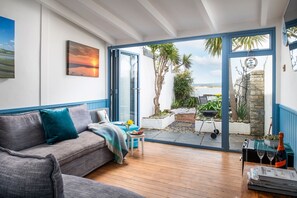 A cozy living room with a sofa, a coffee table, and a view of the outdoors through large glass doors. - 2 Bed cottage in a fantastic waterfront setting (Appledore)