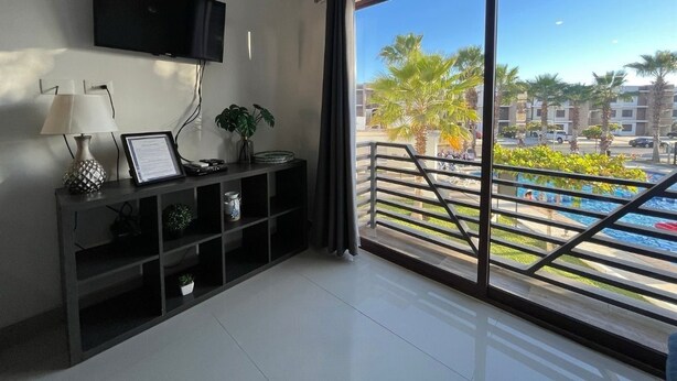 Uma sala de estar moderna com uma televisão grande, uma mesa de consola com objetos decorativos e vista para uma piscina e palmeiras.