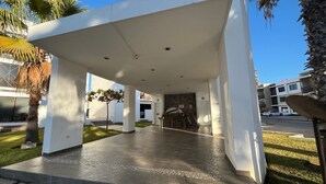 Um edifício moderno com entrada coberta, palmeiras e área pavimentada.