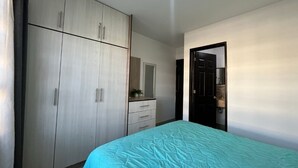 Um quarto com cama, guarda-roupa, cômoda e porta que dá para outro ambiente.