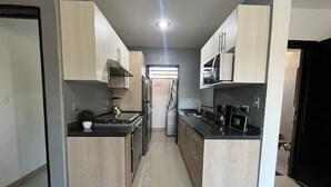 Uma cozinha moderna com armários de madeira clara, bancada preta e eletrodomésticos de aço inoxidável.