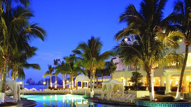 A pool area with palm trees and a view of the ocean at dusk.
