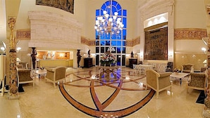 A grand lobby with a central chandelier, ornate columns, and a large stained glass window.