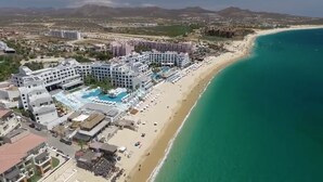 An aerial view of a coastal resort with a large hotel, a sandy beach, and a clear blue sea.