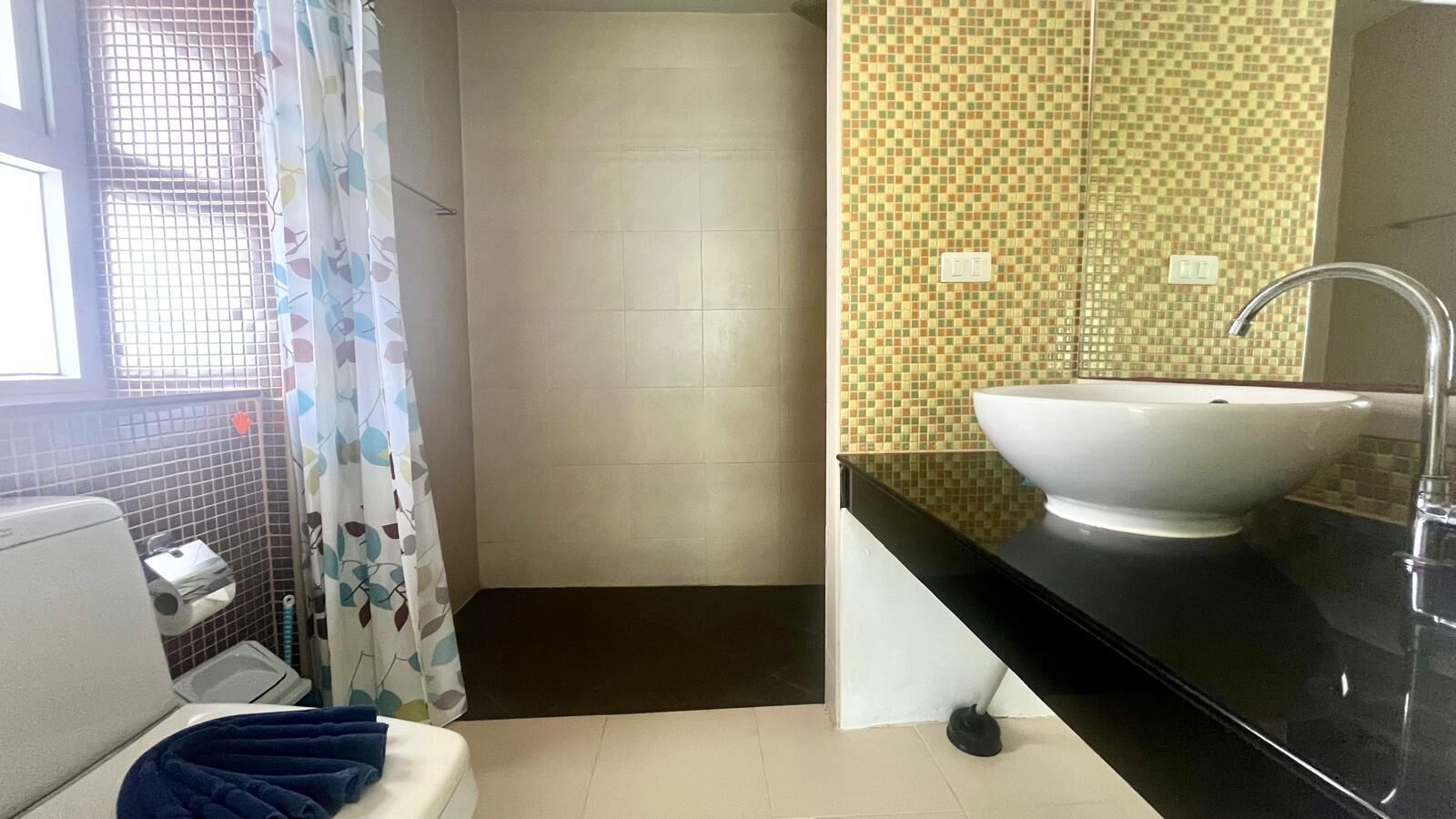 A bathroom with a white sink, black countertop, and a shower curtain with a leaf pattern.