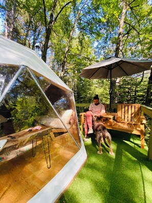 A tent with a clear view of a person sitting on a wooden deck, a dog, and an umbrella. - Ala Glamping (Mudurnu)