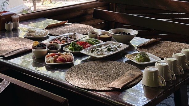 A dining table with various dishes and a view of a forest and yurts through a window. - Ala Glamping (Mudurnu)