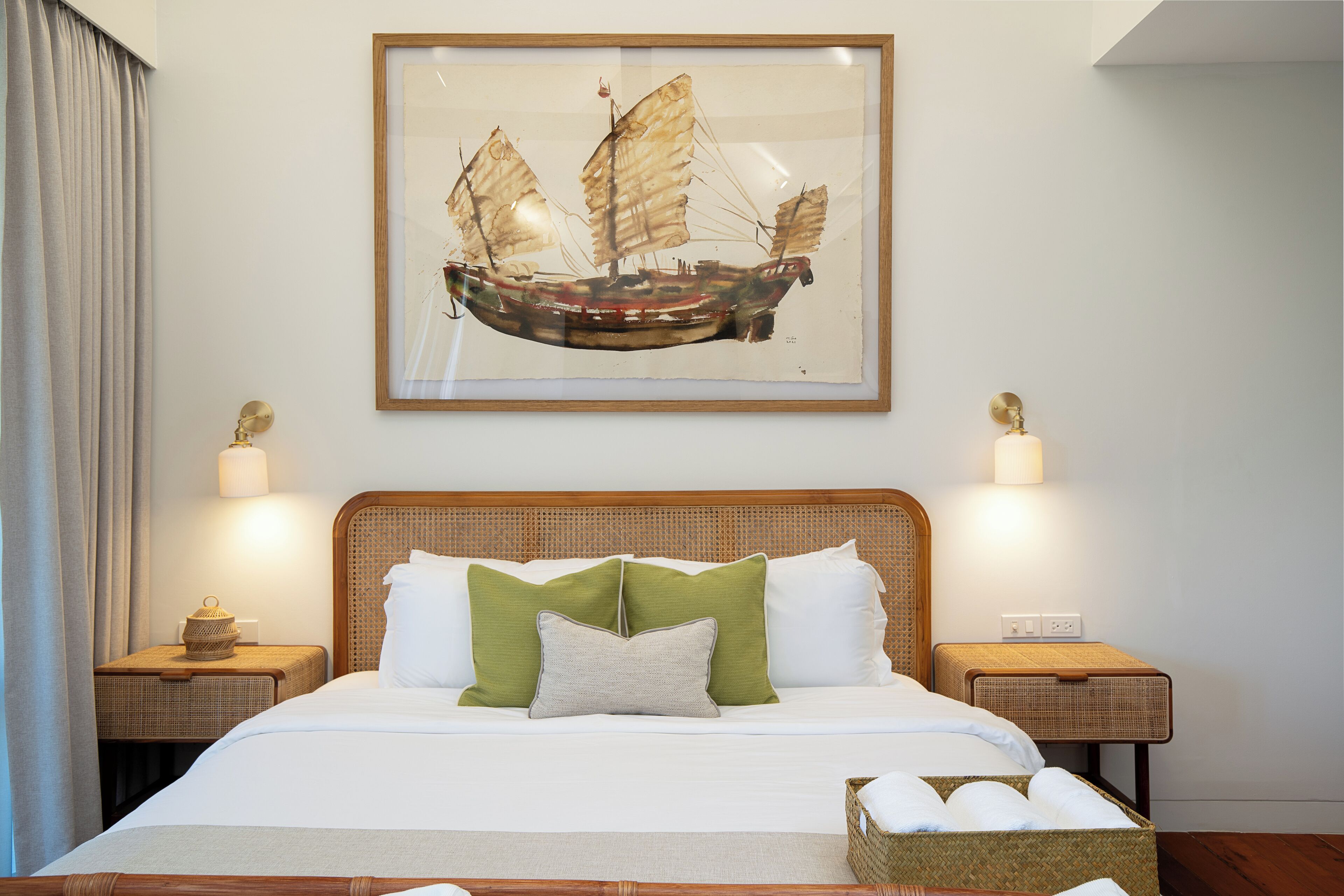 A neatly made bed with white linens and green pillows, a framed artwork of a sailing ship on the wall, and two bedside lamps on wooden nightstands.