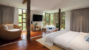 A spacious bedroom with a large bed, a wicker chair, and a television on the wall. - Syama Residence (Ayutthaya)