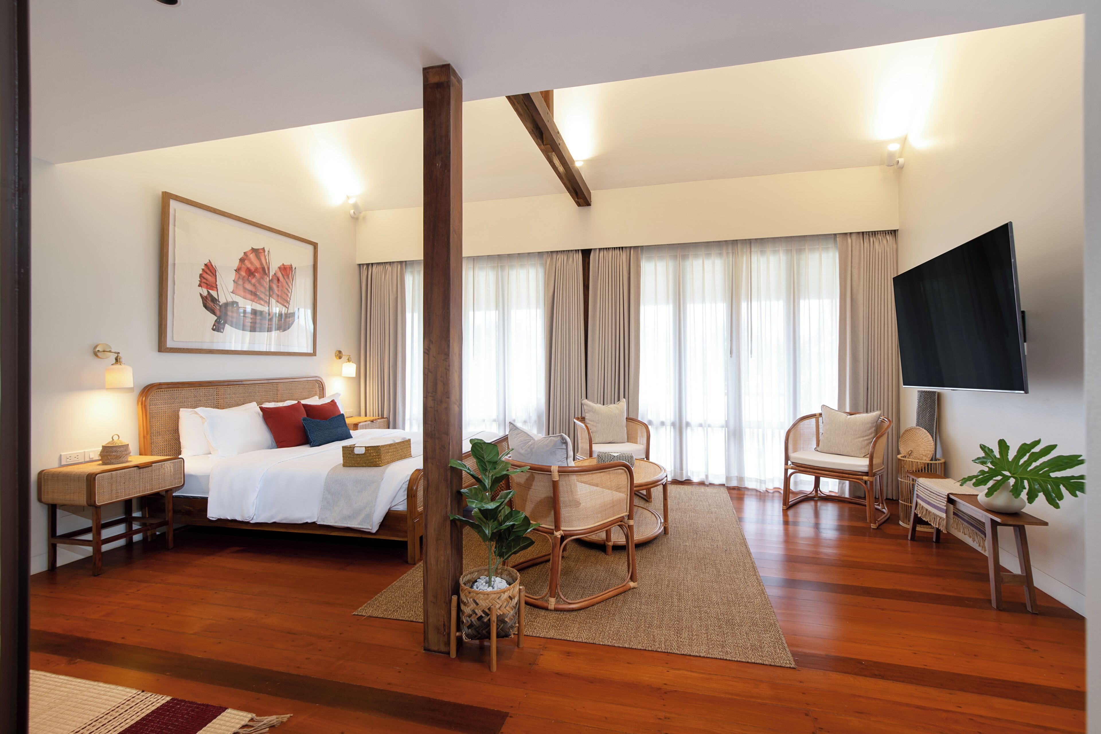 A spacious hotel room with a large bed, a sitting area with chairs, a television, and a large window with curtains.
