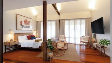 A spacious hotel room with a large bed, a sitting area with chairs, a television, and a large window with curtains.