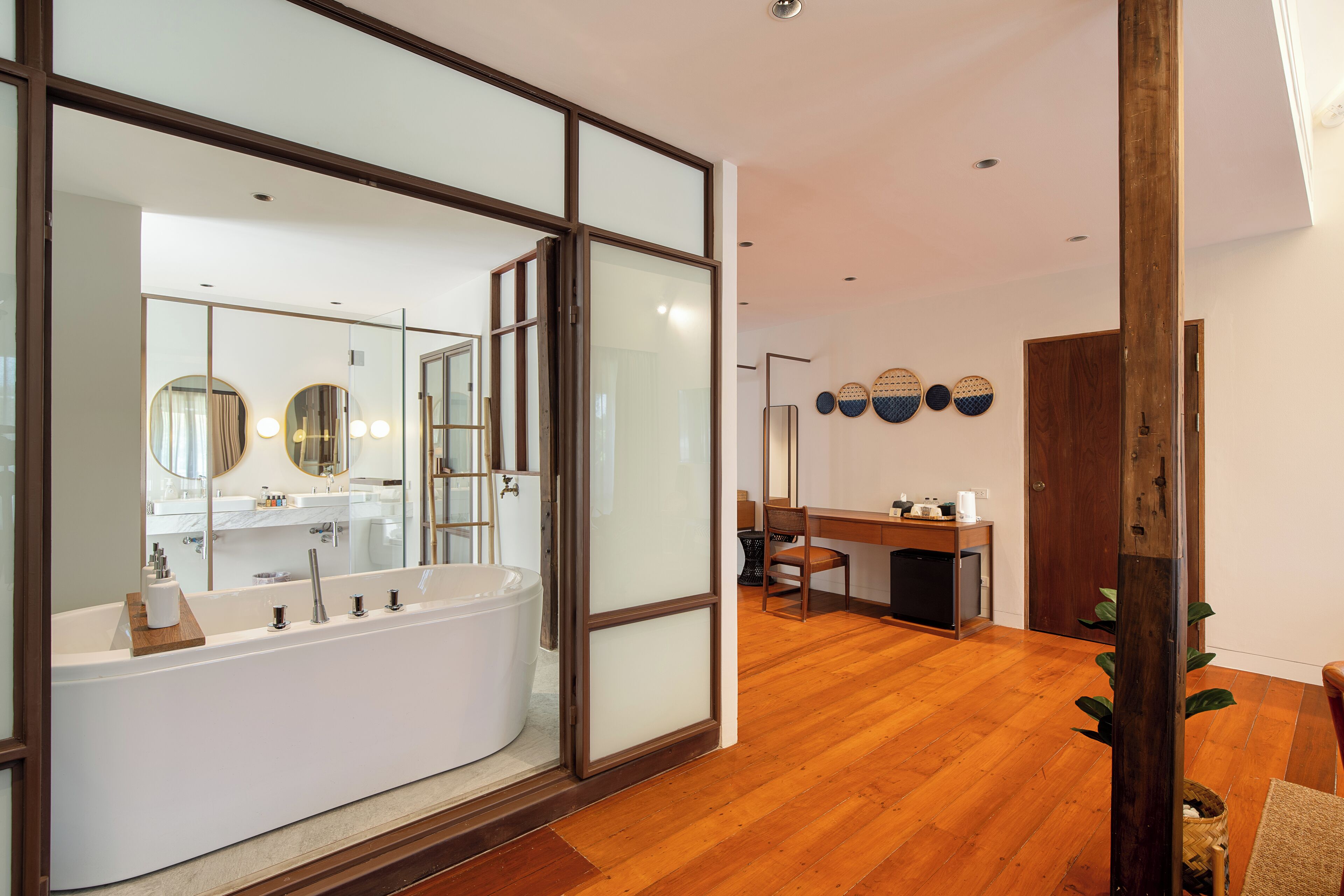 A modern bathroom with a large bathtub, a mirror, and a wooden floor.