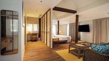 A hotel room with a bed, a television, a seating area with a wicker sofa, and a wooden floor.
