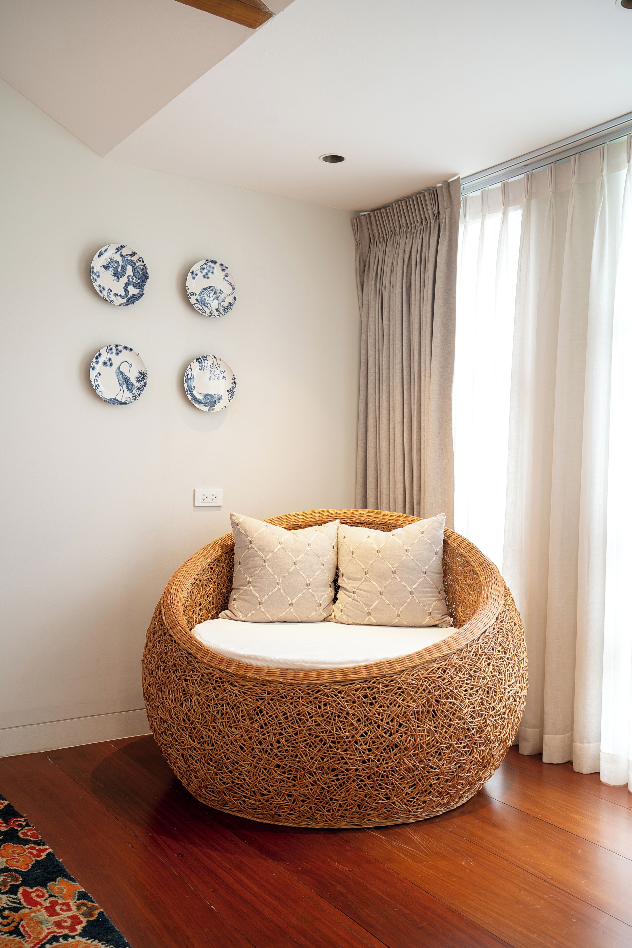 A round wicker chair with cushions, a wooden floor, and four wall-mounted decorative plates.
