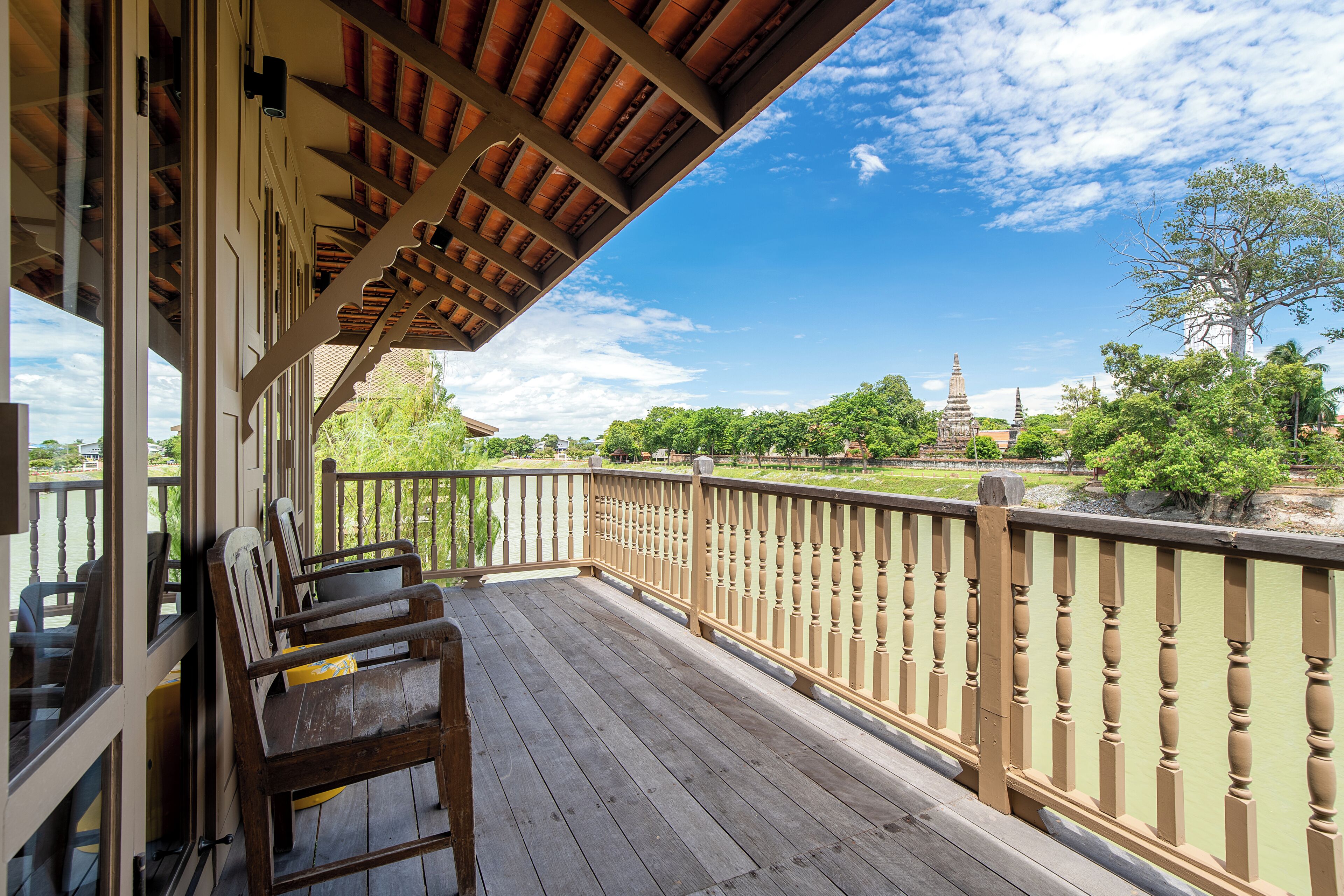 A wooden deck with a railing, overlooking a temple and greenery.