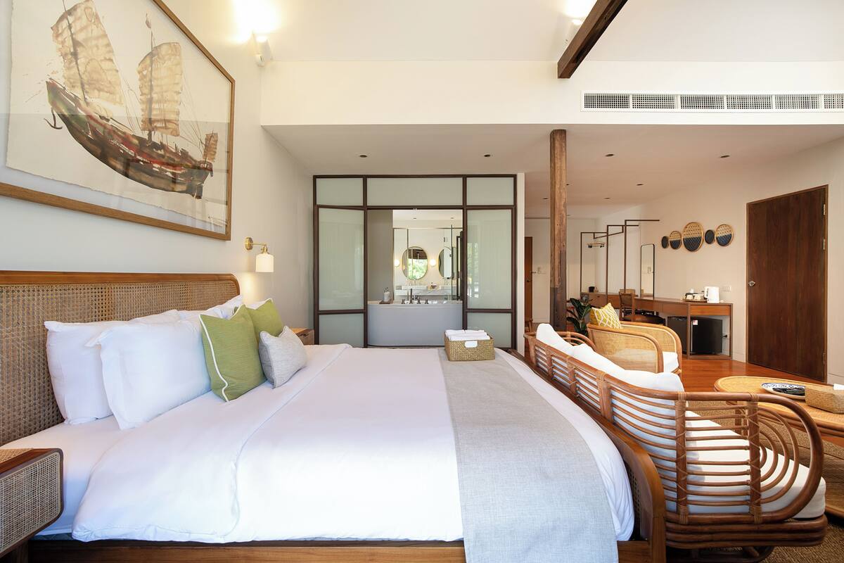 Habitación de hotel con una cama grande, un área de descanso con sillas, un escritorio y un baño visible a través de una puerta de cristal.