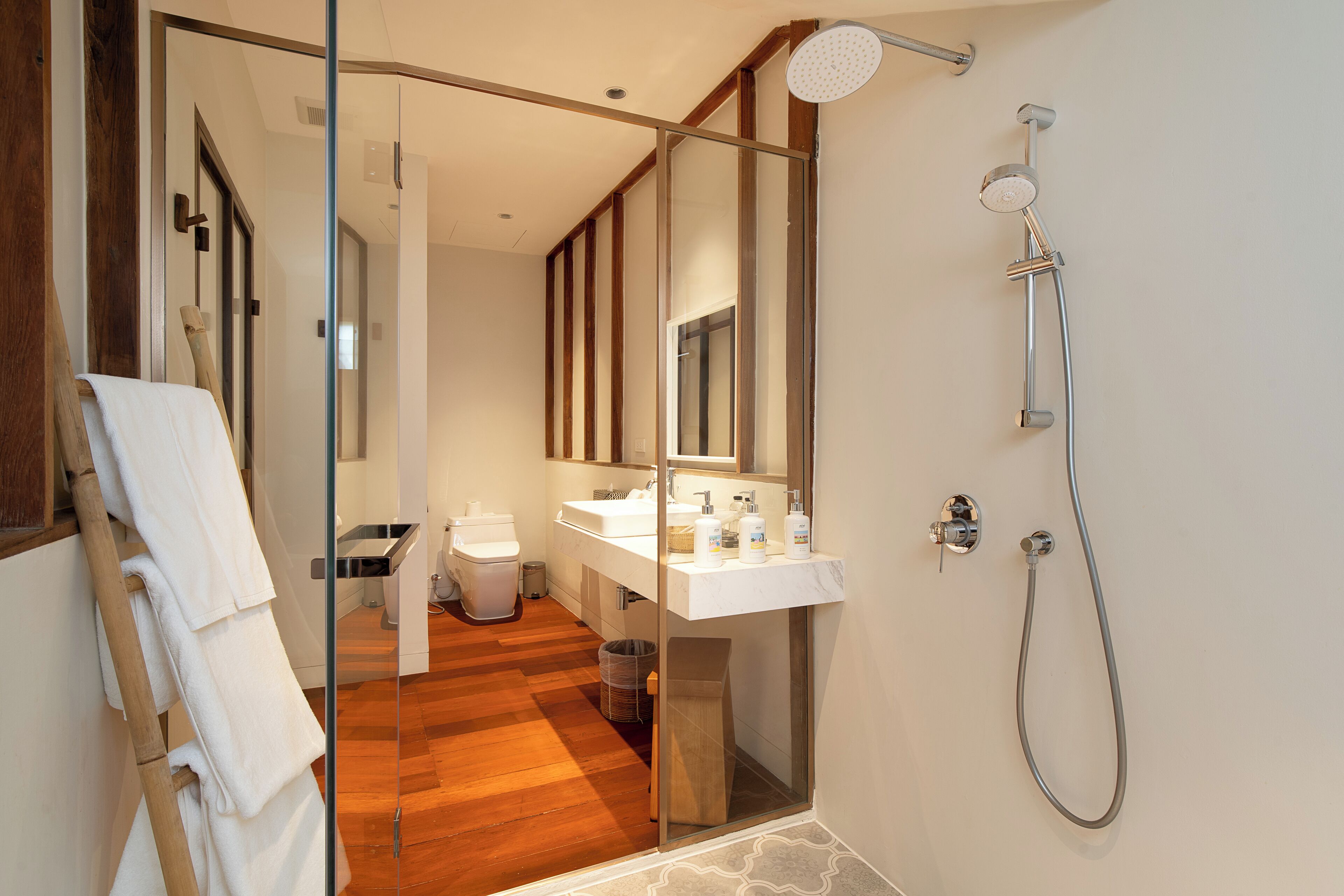 Un baño moderno con cabina de ducha de vidrio, suelo de madera y lavamanos blanco.