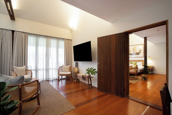 Una sala de estar moderna con piso de madera, un televisor de pantalla plana montado en la pared y una puerta corrediza que da a otra habitación.