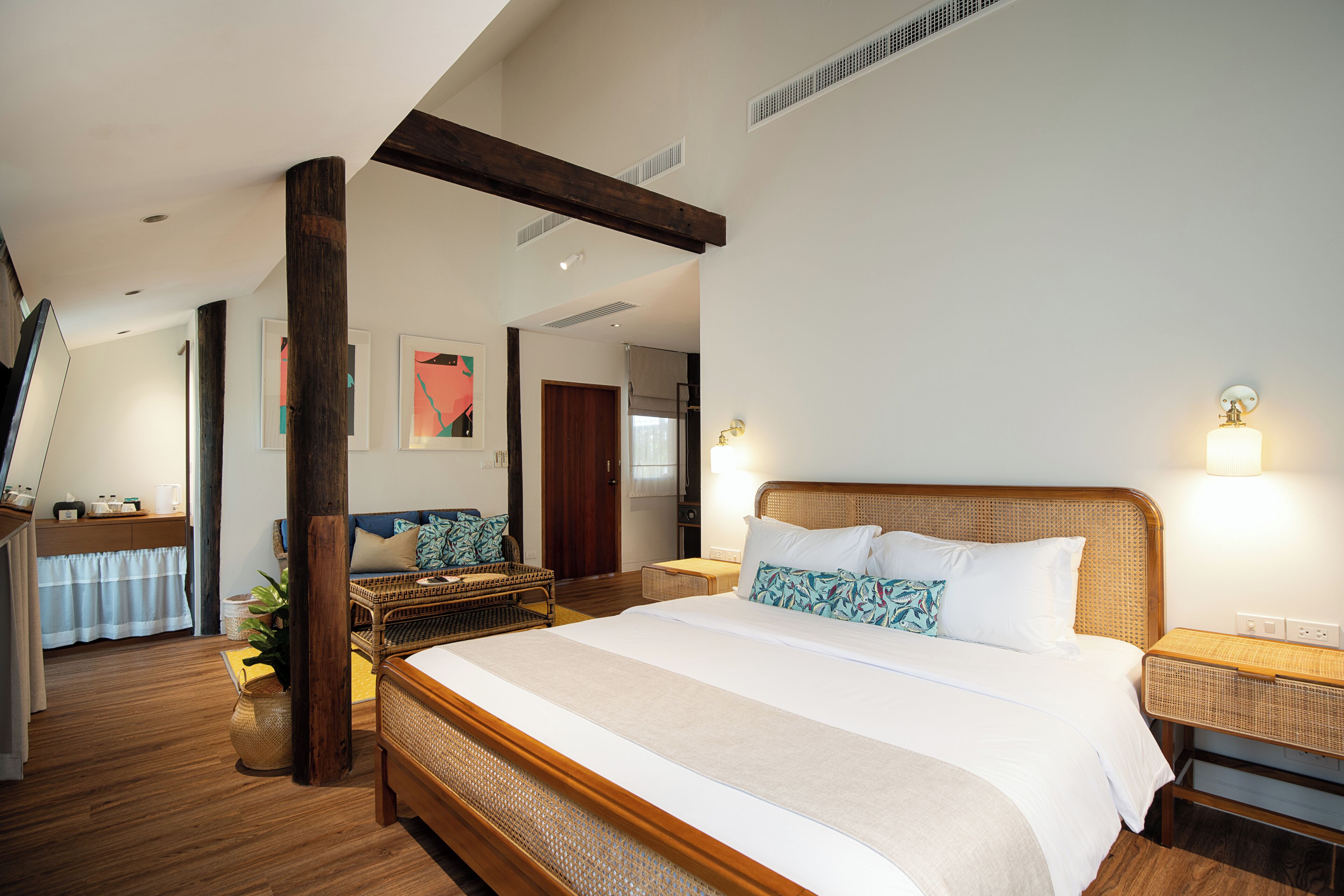 Un dormitorio amplio con una cama grande, vigas de madera, una mesita de mimbre y una lámpara de pared.