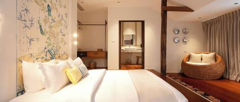 A bedroom with a large bed, a sitting area with a woven chair, a bathroom with a mirror, and a decorative wall.