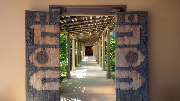 A corridor with a wooden door at the end, leading to a covered area with columns. - Syama Residence (Ayutthaya)