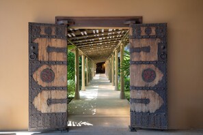 Un pasillo con una puerta de madera al final, que conduce a una zona techada con columnas.