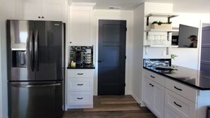 Une cuisine moderne avec des meubles blancs, un réfrigérateur en acier inoxydable et un plan de travail noir.