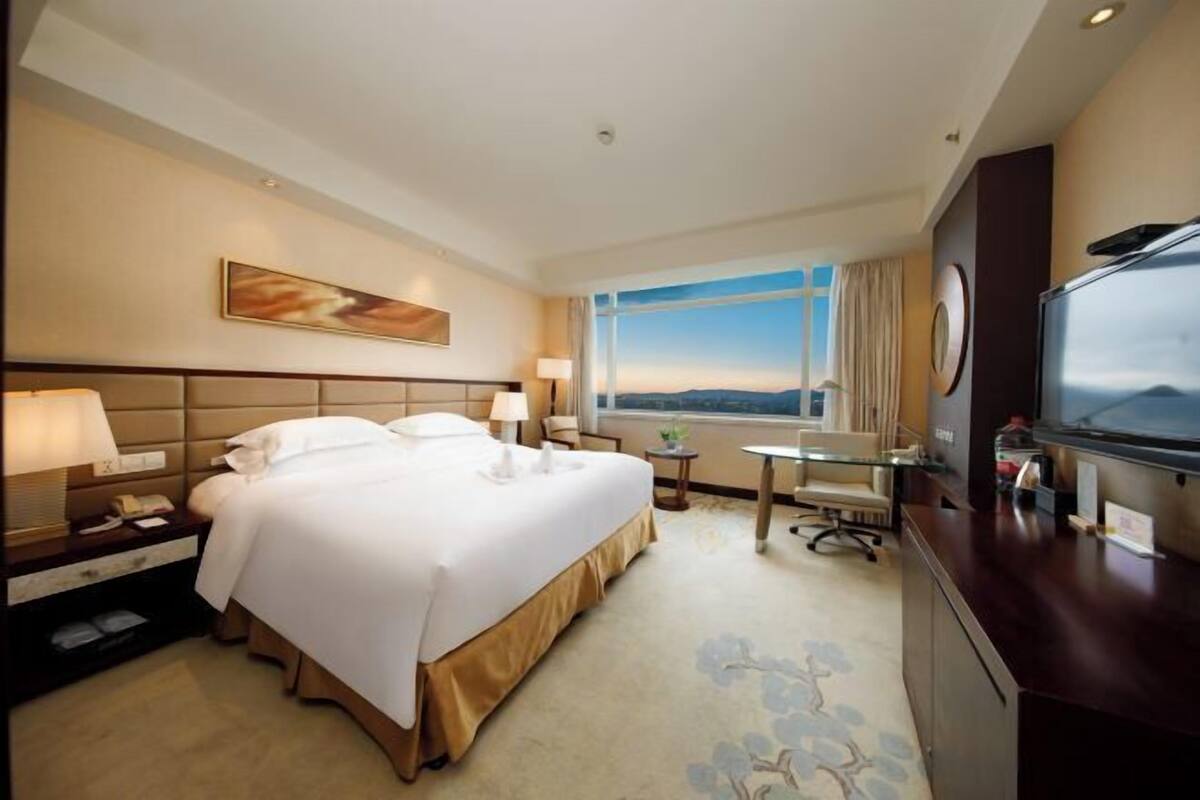 A hotel room with a bed, bedside tables, a desk, a chair, a TV, and a window with a view.