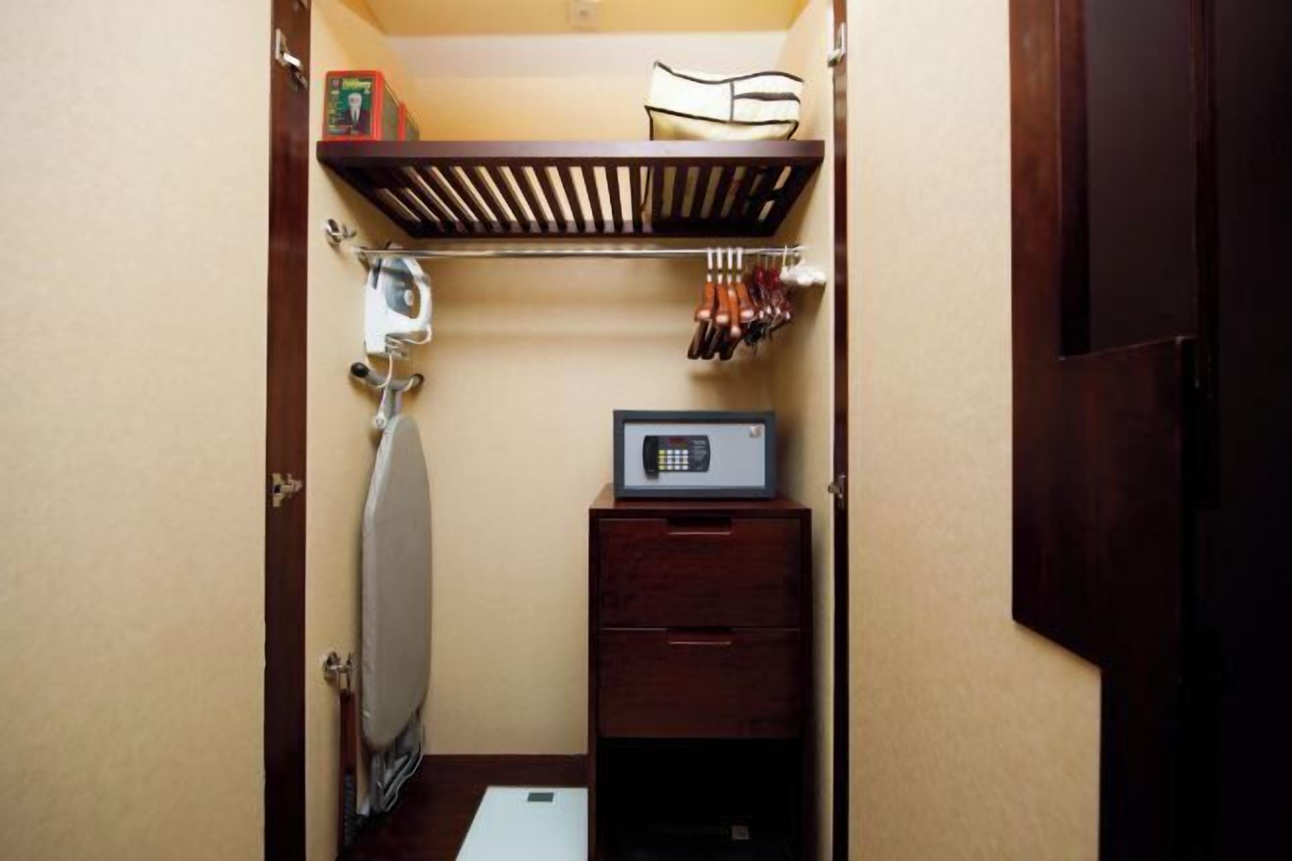 A compact room with a built-in ironing board, a microwave, and a small wooden cabinet.