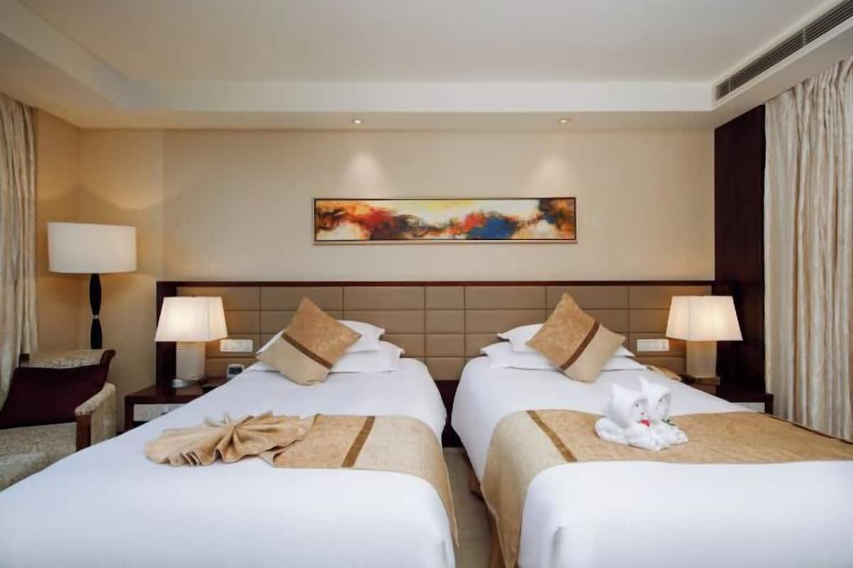 A hotel room with two beds, a painting on the wall, and a cat on one bed.