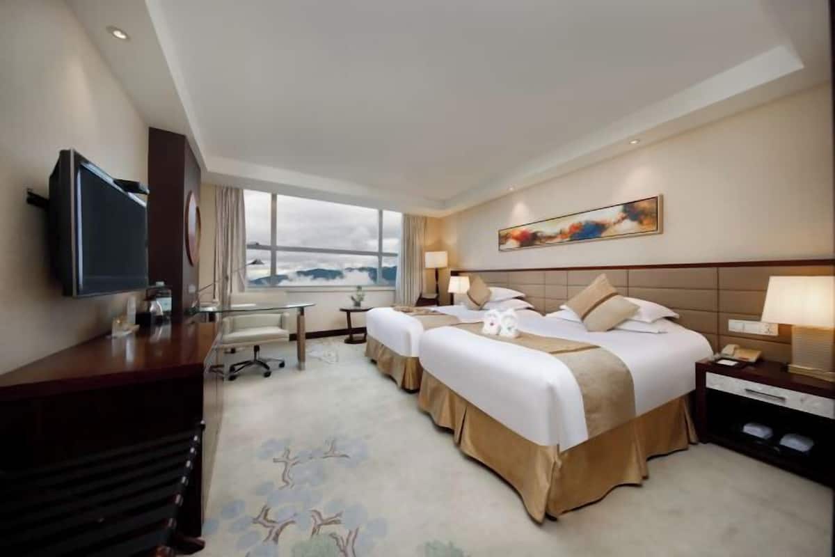 A hotel room with a large bed, a desk, a TV, and a window with a view of the mountains.