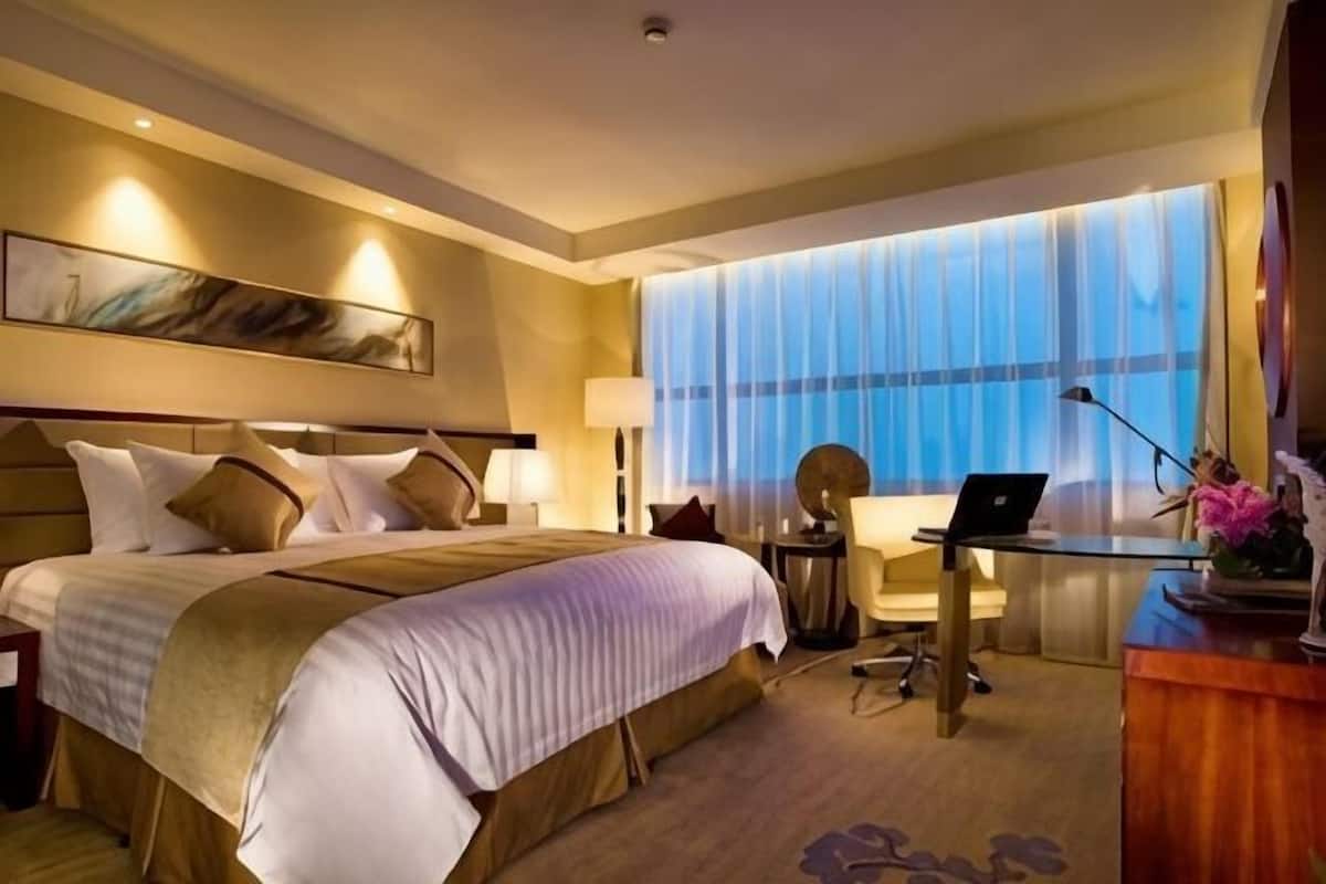 A hotel room with a large bed, a desk with a laptop, a chair, and a window with curtains.