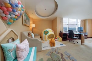 Habitación de hotel con cama, escritorio, silla, ventana con vistas y una decoración de globos de colores.