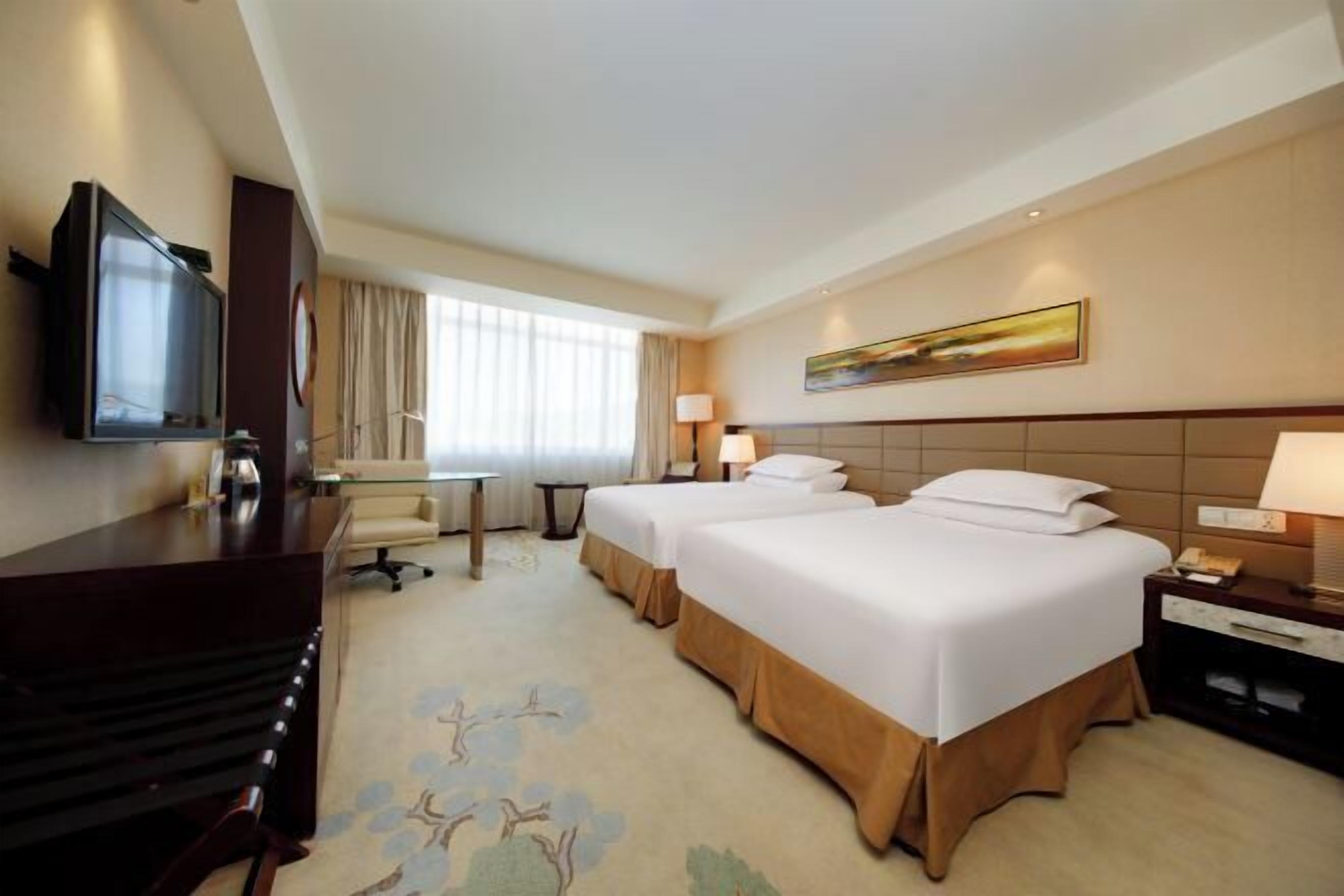 A hotel room with two beds, a desk, a television, and a window with curtains.
