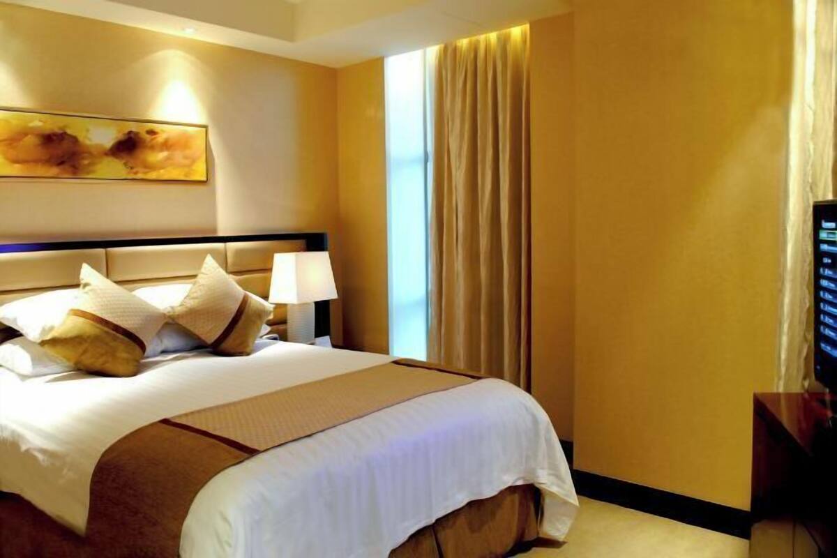 A hotel room with a bed, a nightstand, a lamp, a television, and a large window with curtains.